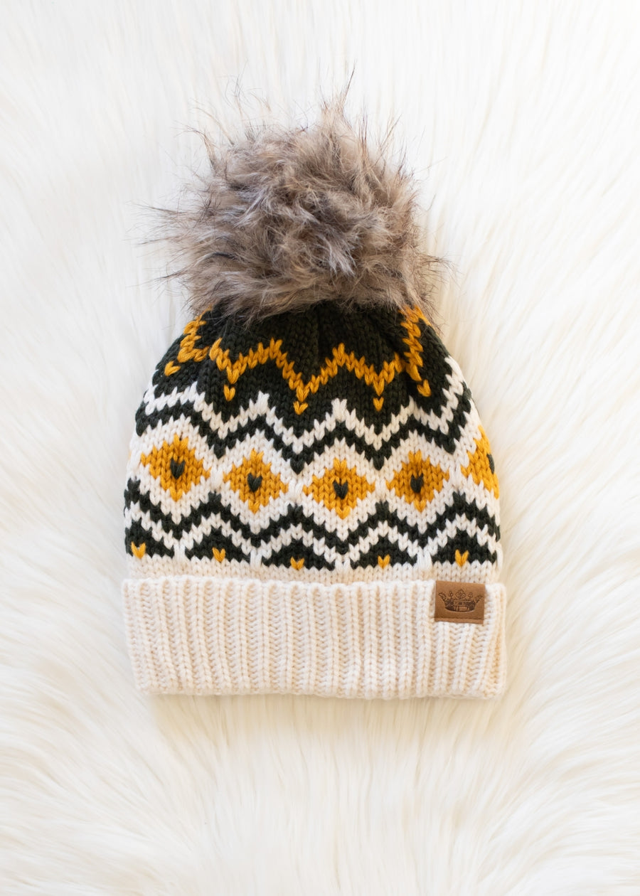 Knit beanie with a pattern and fur pom-pom on a white surface