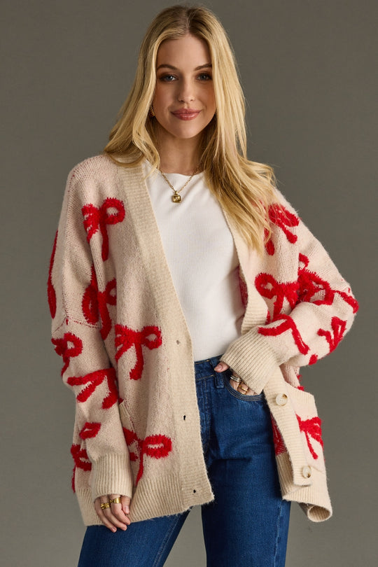 Woman wearing a beige cardigan with red bow patterns on a gray background