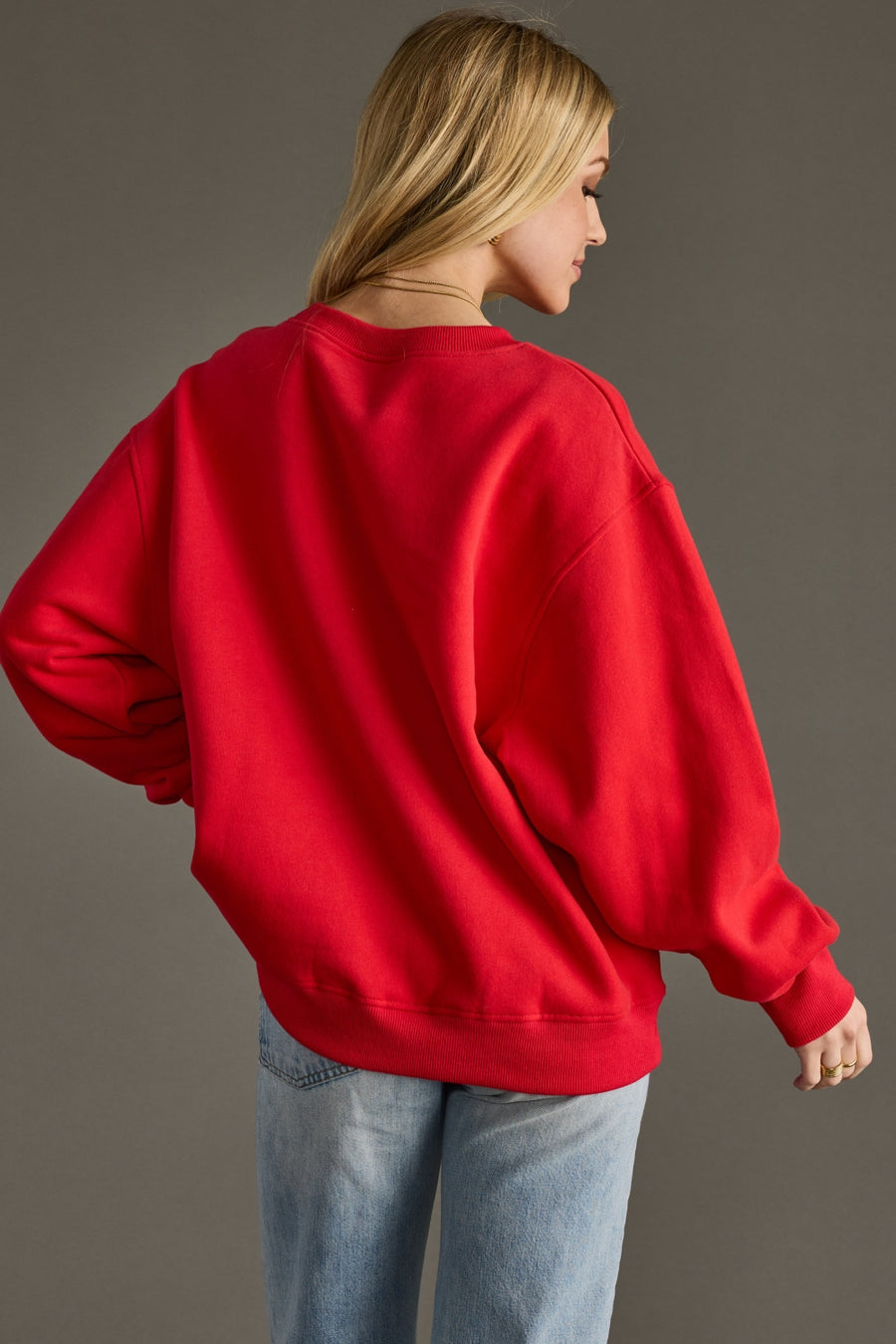 Person wearing a red sweatshirt and blue jeans against a gray background
