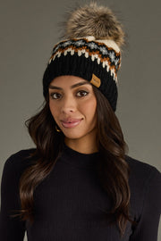 Woman wearing a black knit beanie with a fur pom-pom against a gray background