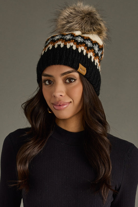 Woman wearing a black knit beanie with a fur pom-pom against a gray background