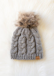 Gray knit beanie with fur pom-pom on a white background
