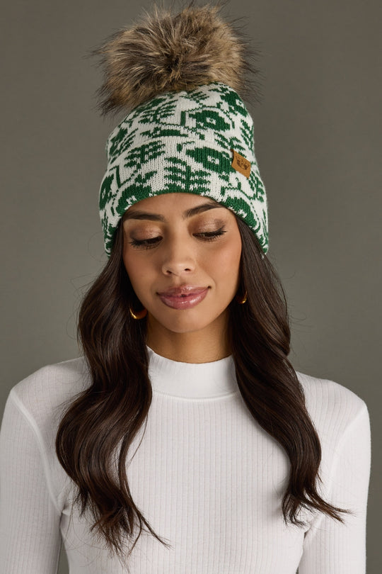 Woman wearing a green and white patterned beanie with a pom-pom on a gray background