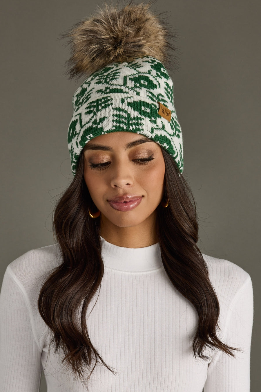 Woman wearing a green and white patterned beanie with a pom-pom on a gray background