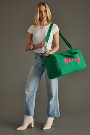 Woman holding a green duffel bag with pink text against a gray background