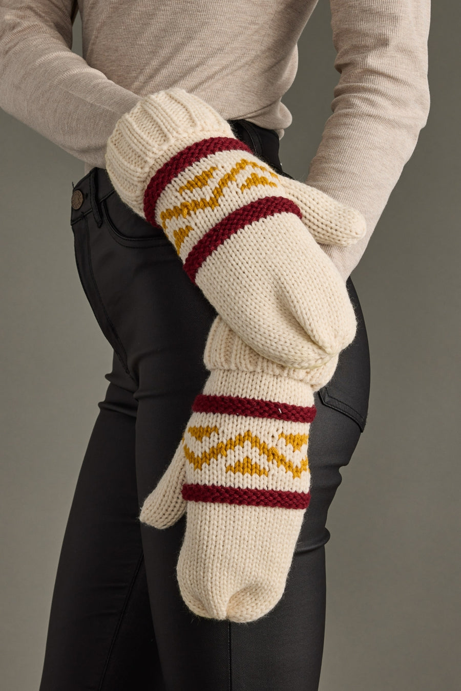 Knitted mittens with a pattern held by a person against a neutral background