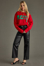 Woman wearing a red sweater with 'Merry' text, black pants, and high heels on a gray background