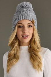 Woman wearing a gray knit beanie with a pom-pom against a neutral background