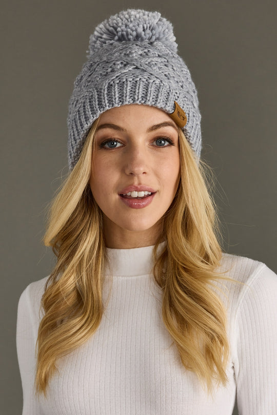 Woman wearing a gray knit beanie with a pom-pom against a neutral background