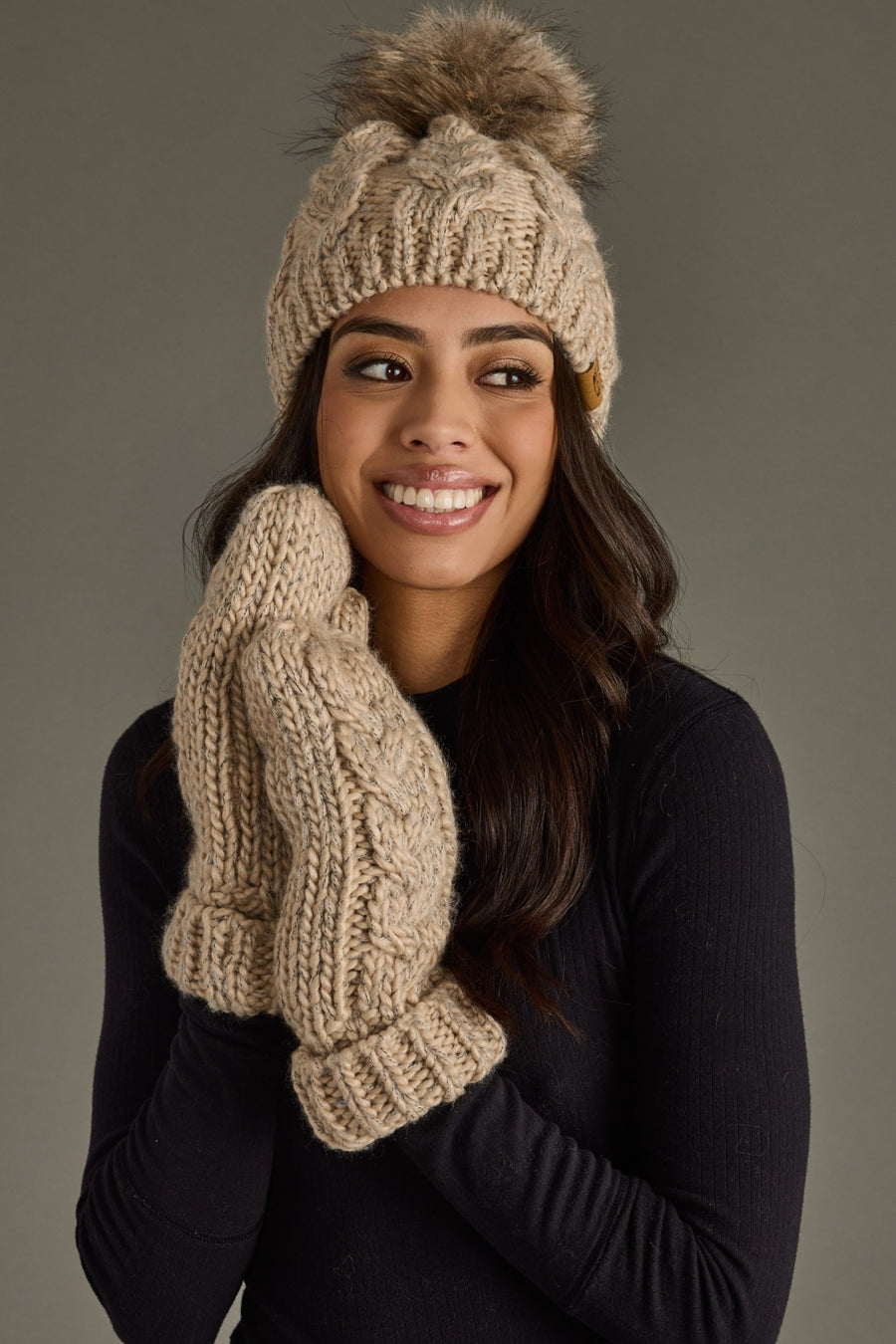 Woman wearing a beige knit hat and mittens against a gray background