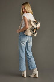 Woman wearing a patterned backpack and light blue jeans on a gray background