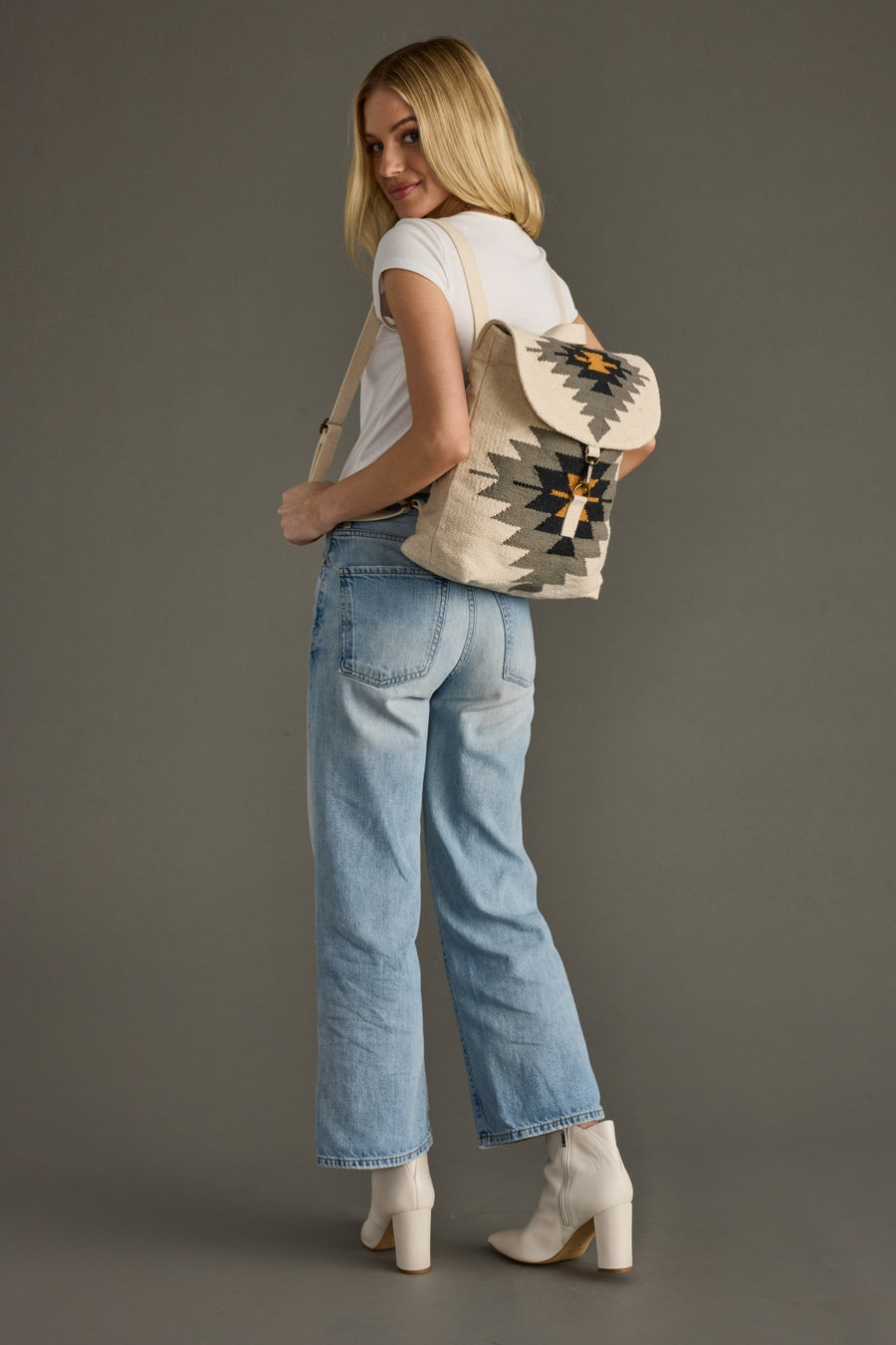 Woman wearing a patterned backpack and light blue jeans on a gray background