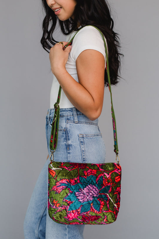 Woman holding a colorful floral-patterned crossbody bag against a gray background