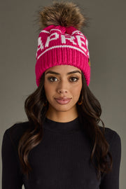 Woman wearing a pink knit beanie with a pom-pom on a gray background