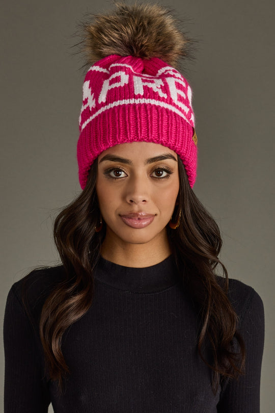 Woman wearing a pink knit beanie with a pom-pom on a gray background