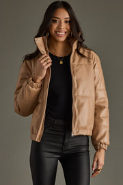 Woman wearing a tan jacket holding a phone against a gray background