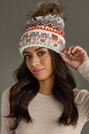 Woman wearing a patterned beanie with a fur pom-pom against a gray background