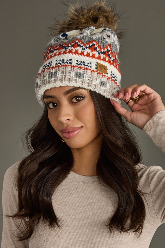 Woman wearing a patterned beanie with a fur pom-pom against a gray background