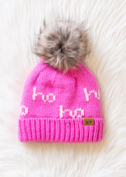 Pink knit beanie with fur pom-pom on a white fur background