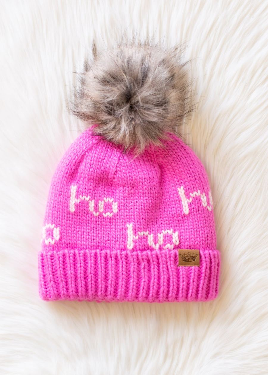 Pink knit beanie with fur pom-pom on a white fur background