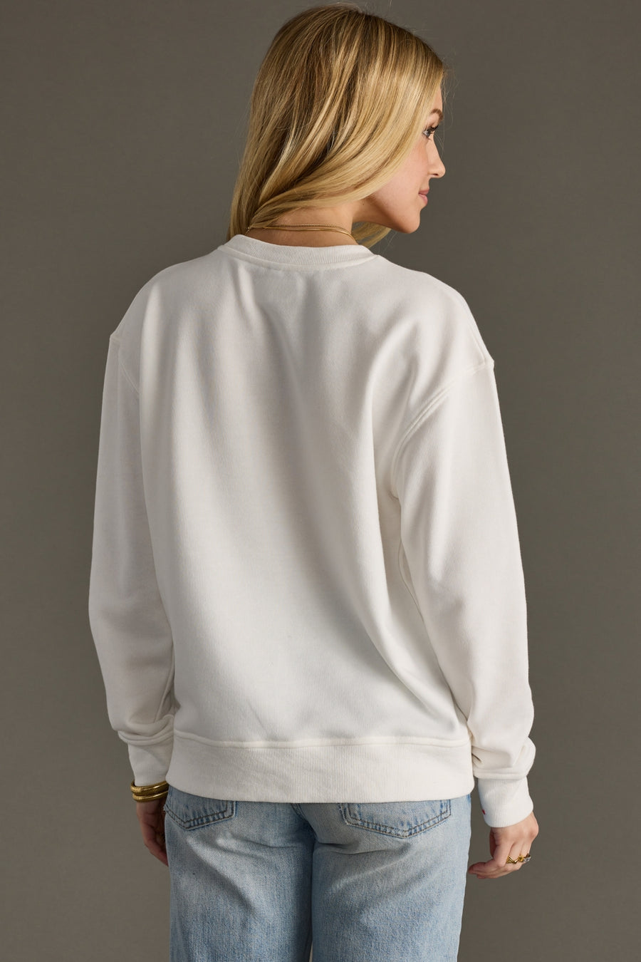 Person wearing a light gray sweatshirt and blue jeans against a plain background