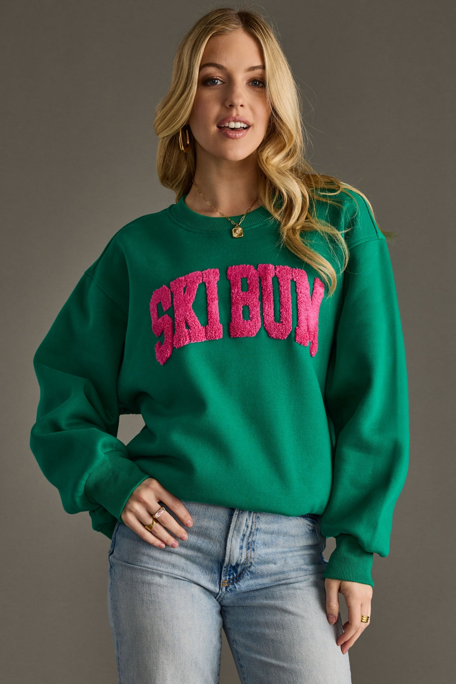 Woman wearing a green sweatshirt with 'Ski Bum' in pink text against a gray background
