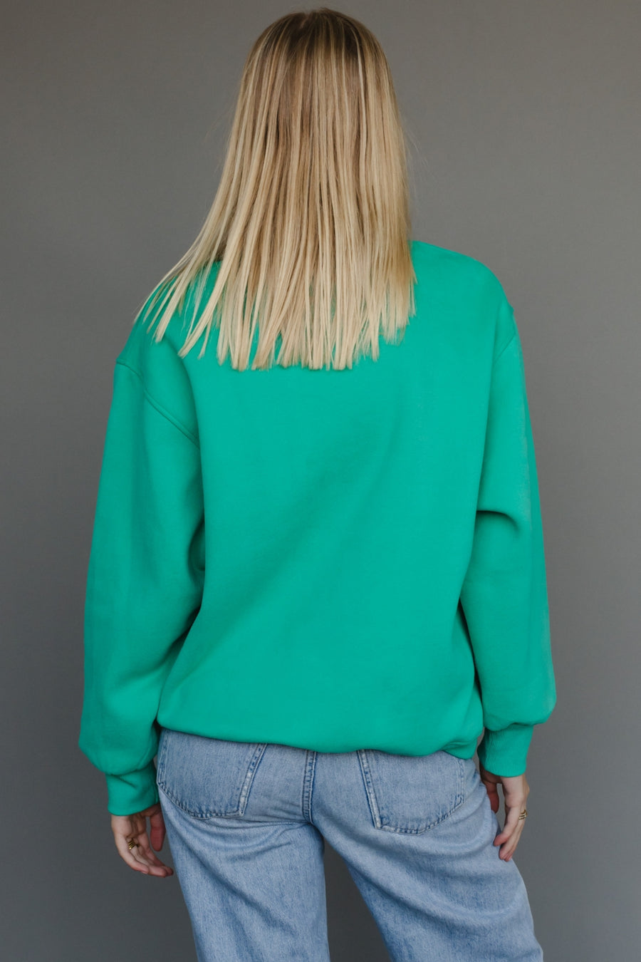 Person wearing a teal sweatshirt and blue jeans against a gray background