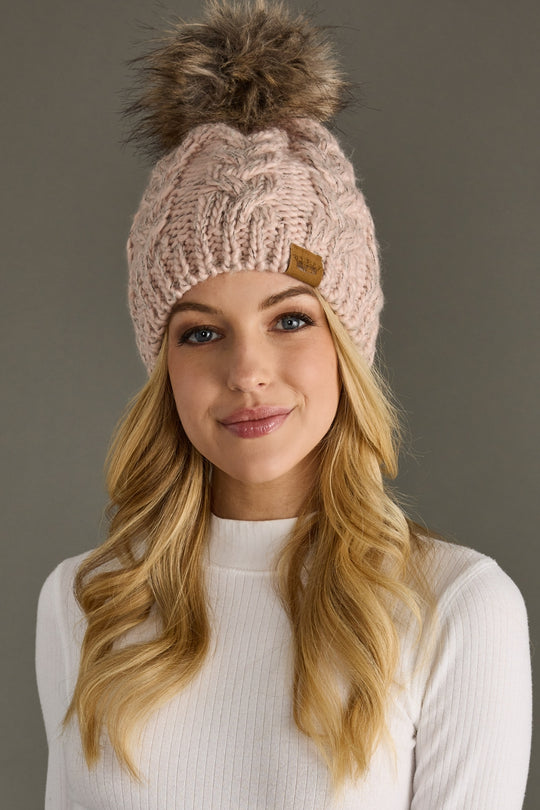 Woman wearing a beige knit beanie with a pom-pom against a gray background