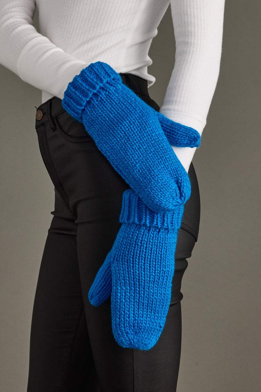 Blue knitted mittens worn by a person against a neutral background
