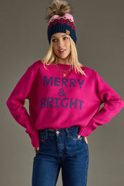 Person wearing a pink sweater with 'MERRY & BRIGHT' text, blue jeans, and a festive hat on a gray background