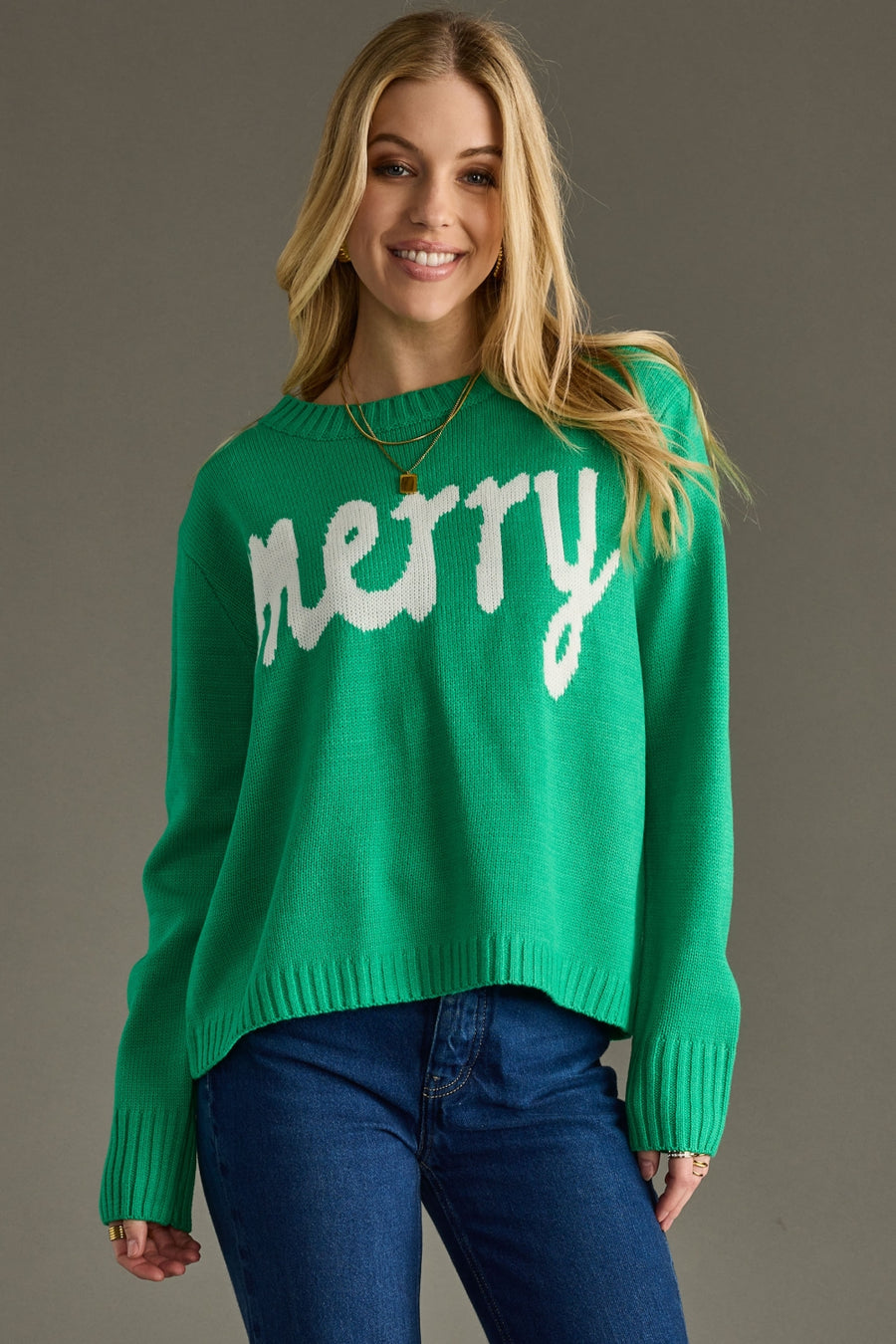Woman wearing a green sweater with 'merry' text on a gray background