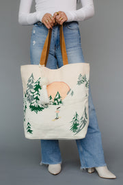 Person holding a tote bag with winter scene design against a gray background