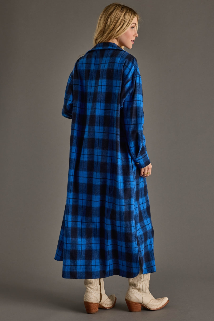 Woman wearing a long blue plaid coat against a gray background