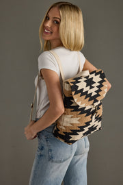 Woman wearing a black and beige patterned backpack against a gray background