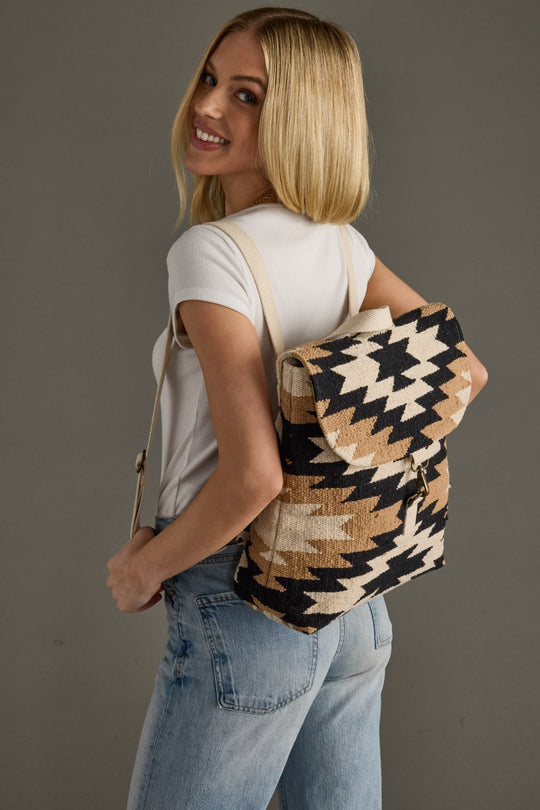 Woman wearing a black and beige patterned backpack against a gray background