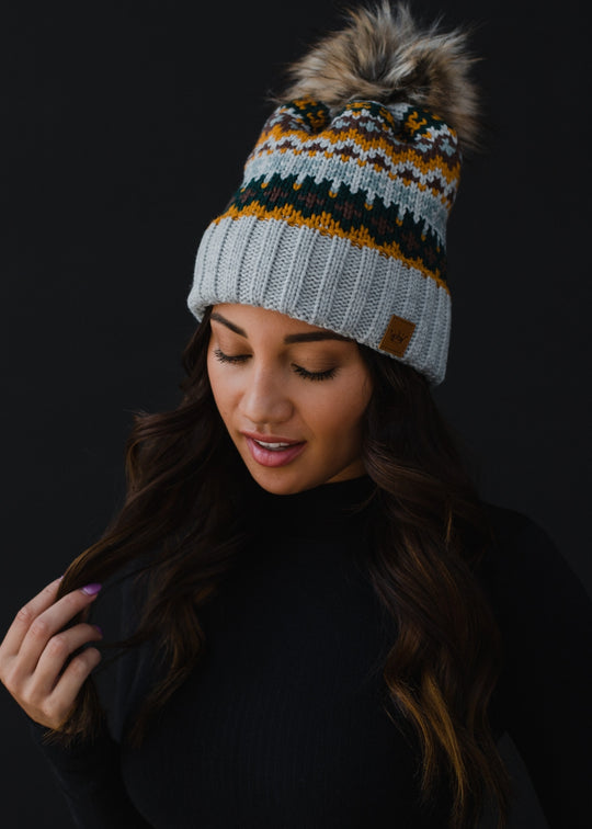 Woman wearing a patterned knit beanie with a pom-pom against a black background