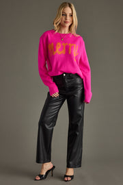 Woman wearing a bright pink sweater with yellow text and black pants on a gray background