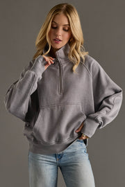 Woman wearing a gray pullover with a quarter zip design against a gray background