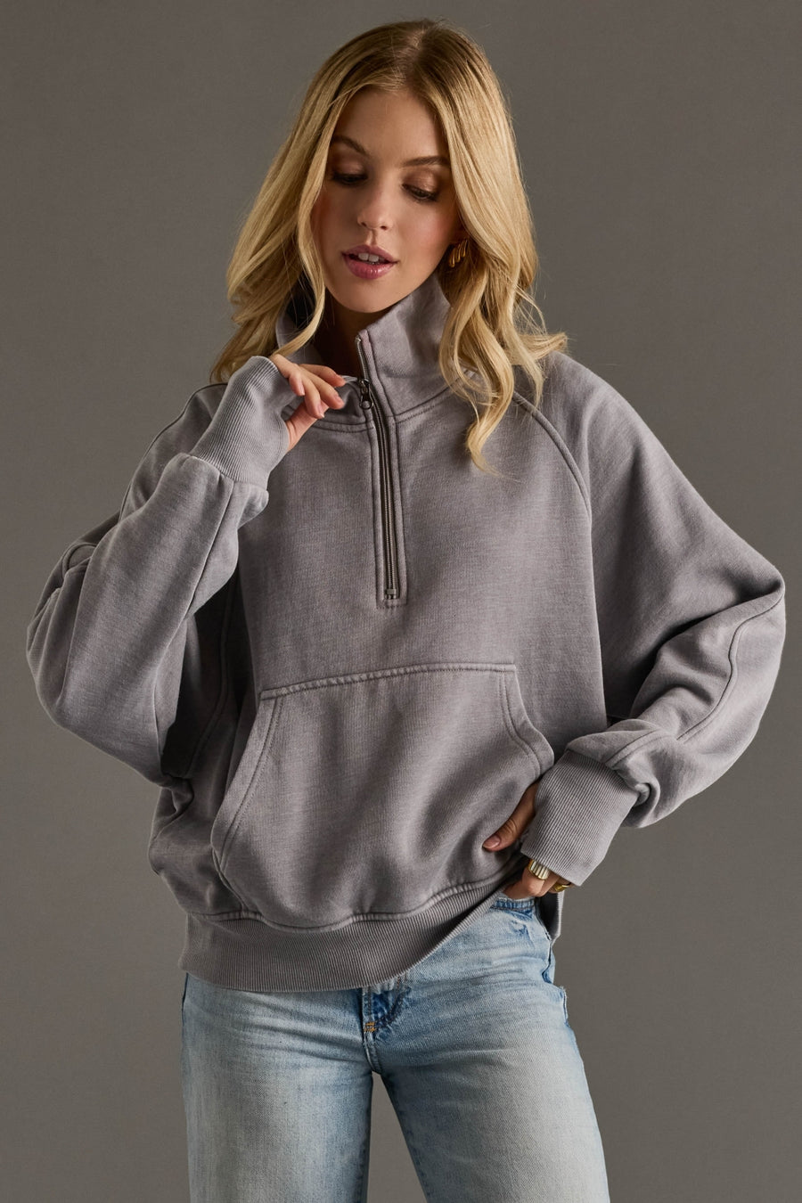 Woman wearing a gray pullover with a quarter zip design against a gray background