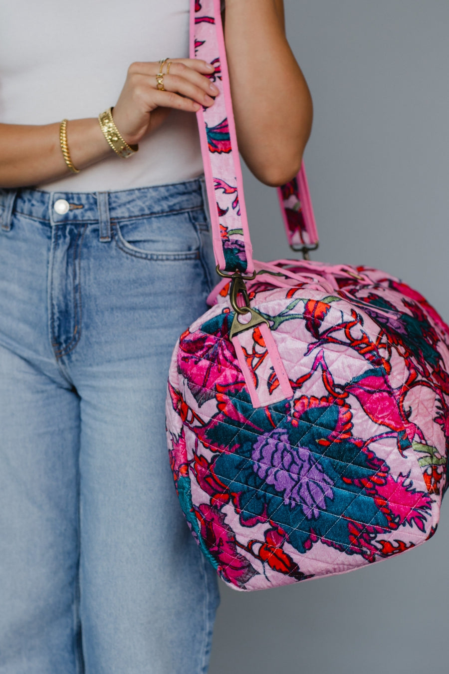 Person holding a colorful quilted bag with a pink strap against a plain background