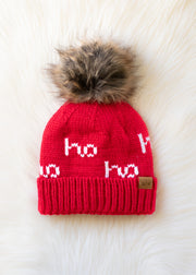 Red knit beanie with fur pom-pom and 'ho ho ho' text on a white background