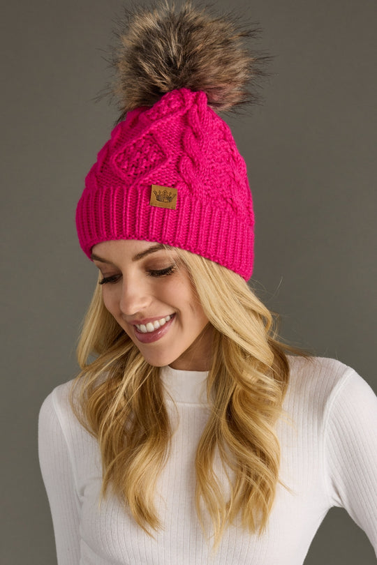 Woman wearing a bright pink knit beanie with a fur pom-pom on a gray background