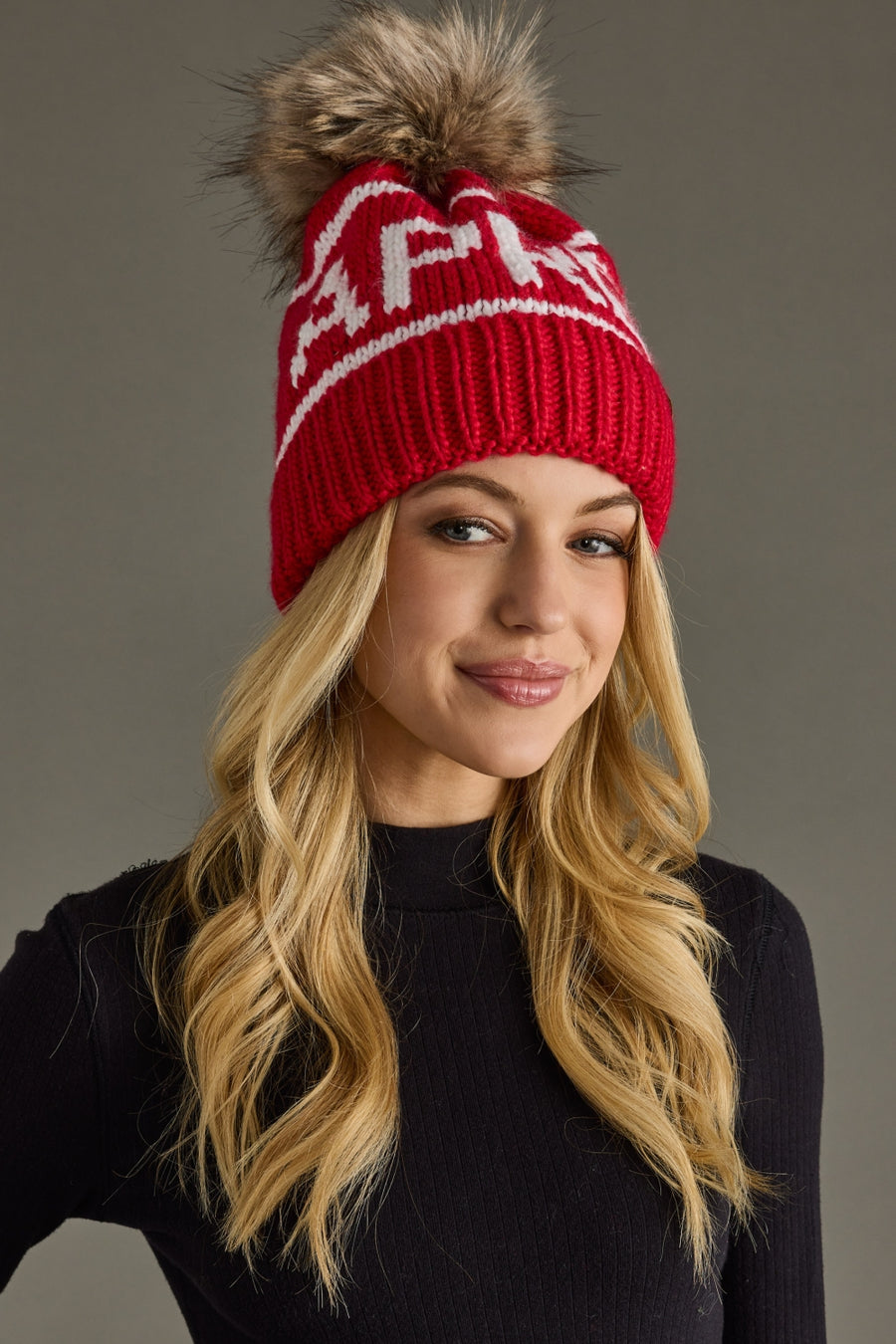 Woman wearing a red knit hat with a pom-pom on a gray background