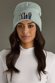 Woman wearing a light blue beanie with colorful text and symbols on a gray background