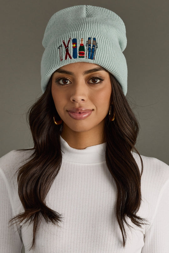 Woman wearing a light blue beanie with colorful text and symbols on a gray background