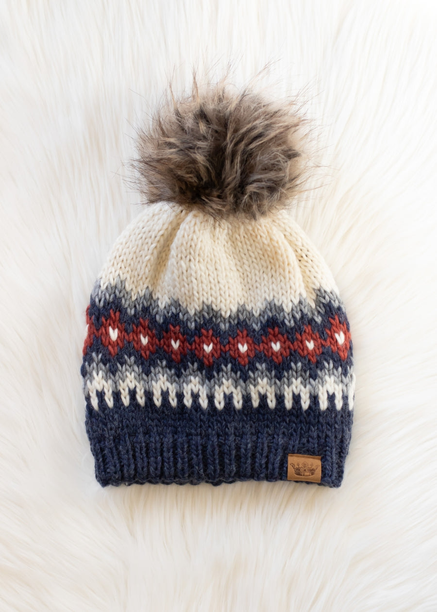 Knit beanie with a pom-pom on a light wooden surface