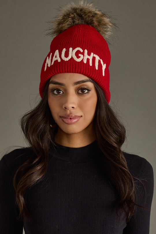 Woman wearing a red beanie with 'NAUGHTY' text against a gray background