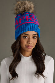 Woman wearing a blue knit beanie with a fur pom-pom on a gray background