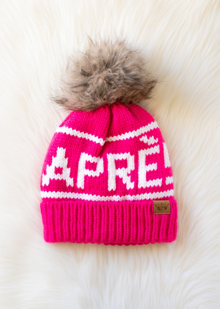 Pink knit beanie with white text and fur pom-pom on a light background