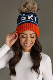 Woman wearing a colorful knit beanie with a fur pom-pom on a gray background